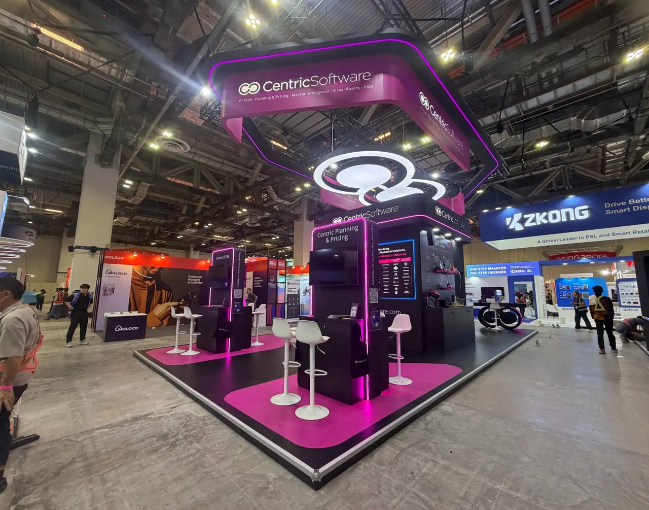 Black and magenta Centric Software exhibition stand with illuminated overhead branding, interactive screens and meeting areas