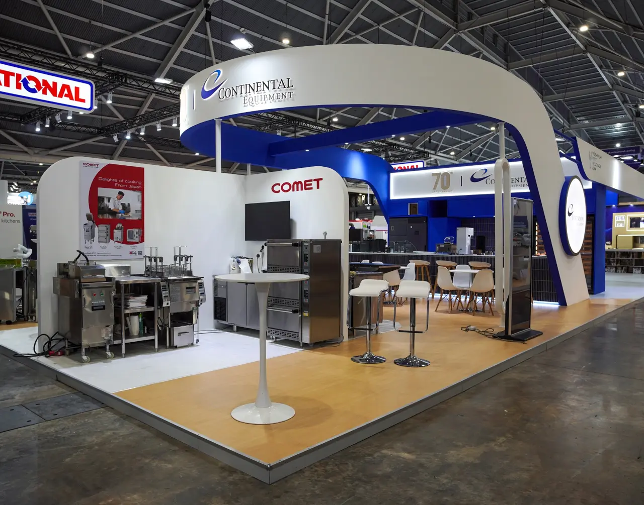 White and blue Continental Equipment exhibition stand with a curved overhead fascia, commercial kitchen equipment and hospitality seating